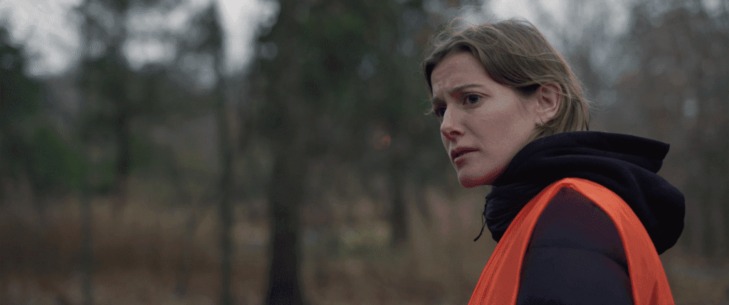a young woman wearing an orange vest looks worryingly off camera