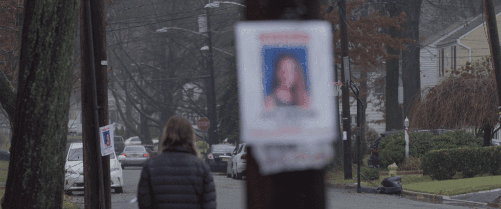 A young woman walks down the street past an out of focus "missing" sign